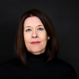 Porträt einer Frau mit langen, dunklen Haaren und einem schwarzen Rollkragenpullover.